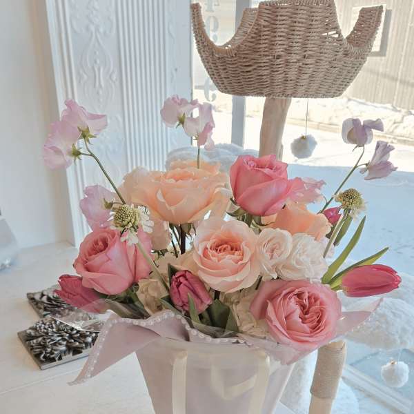 Pink and peach rose bouquet in a white gift bag with a clear macaron box