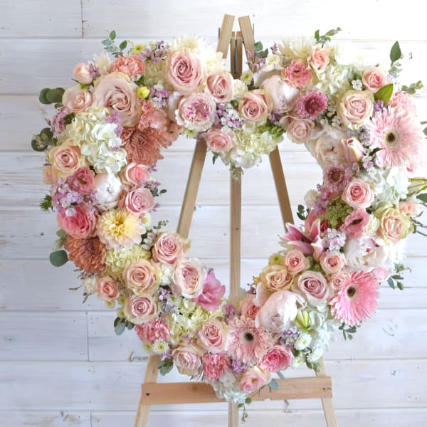Heart-shaped floral wreath on a wooden easel with pink and white flowers