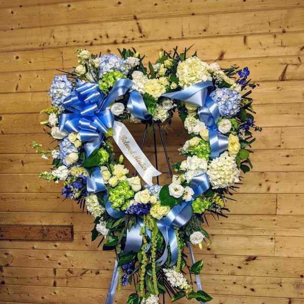 Heart-shaped floral wreath with blue ribbons on a stand
