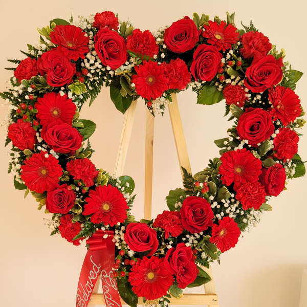 Heart-shaped floral wreath with red roses and gerbera daisies on an easel