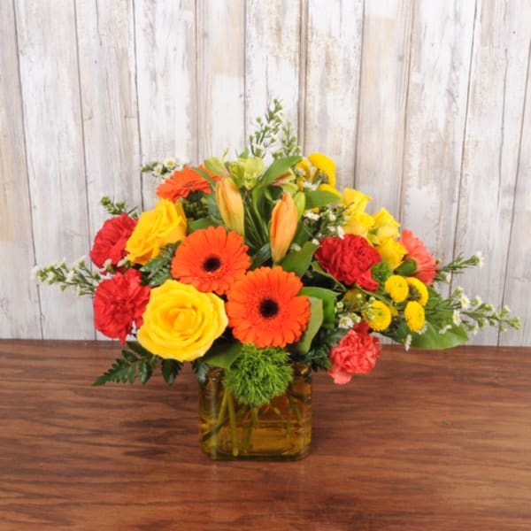 Bright mix of orange, yellow, and red flowers in a yellow glass cube vase