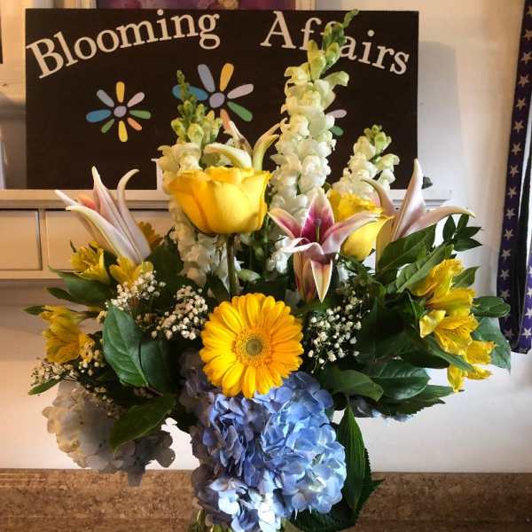 Mixed bouquet with yellow lilies, blue hydrangeas, and a yellow gerbera daisy in a glass vase
