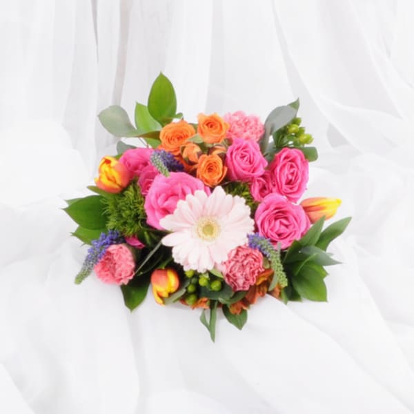 Bright mixed bouquet with pink gerbera, roses, tulips, and carnations on a white fabric backdrop