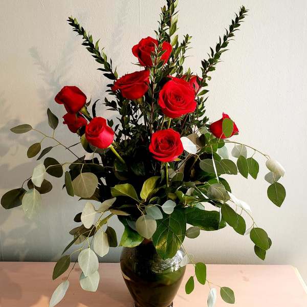 Red roses arranged in a dark glass vase with airy eucalyptus