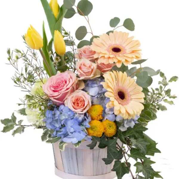 Mixed bouquet in a wooden basket with pink roses, yellow tulips, and peach gerbera daisies