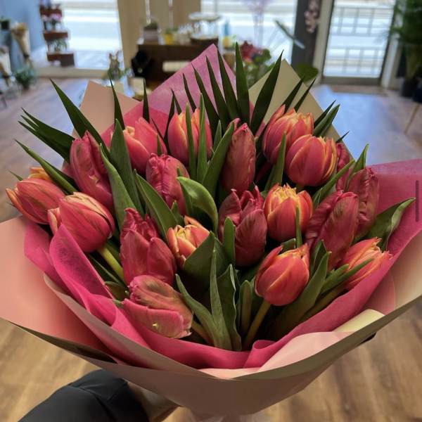 Hand-tied bouquet of pink and orange tulips with tall green foliage in pink and cream wrapping paper.