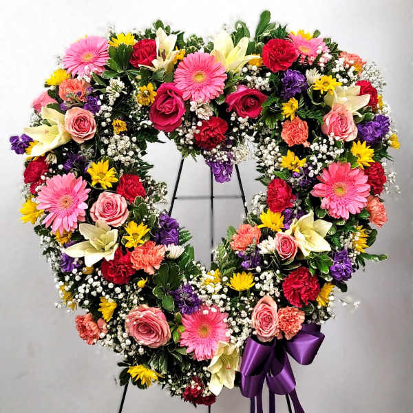 Heart-shaped floral wreath with pink, red, yellow, and white flowers on a stand