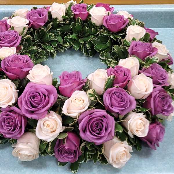 Circular wreath of purple and white roses on a blue surface