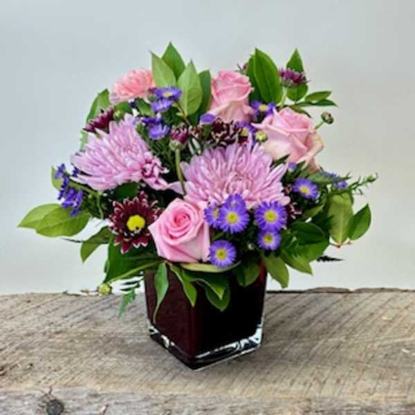 Pink and purple mixed flower arrangement in a square vase