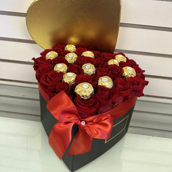 Heart-shaped box of red roses topped with gold-wrapped chocolates and a red ribbon