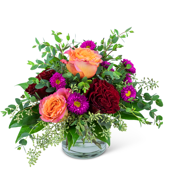 Peach and burgundy roses with purple daisies in a glass vase