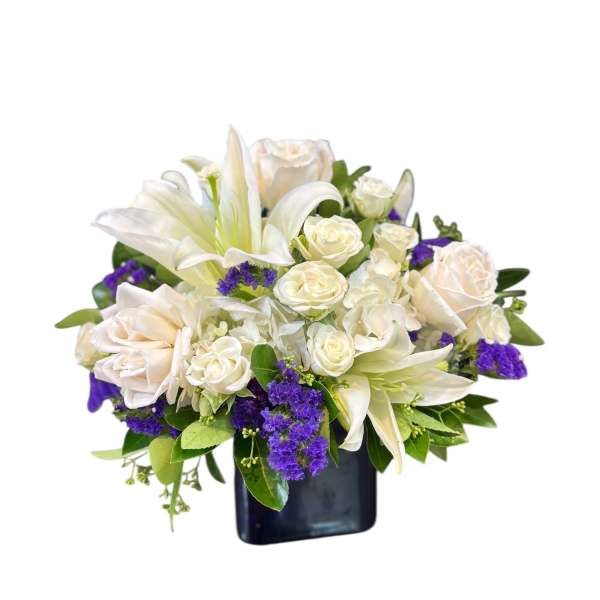 White lilies and roses arranged in a dark vase with purple accents