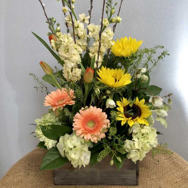 Mixed floral arrangement with sunflowers, gerbera daisies, tulips, and pale blooms in a wooden box