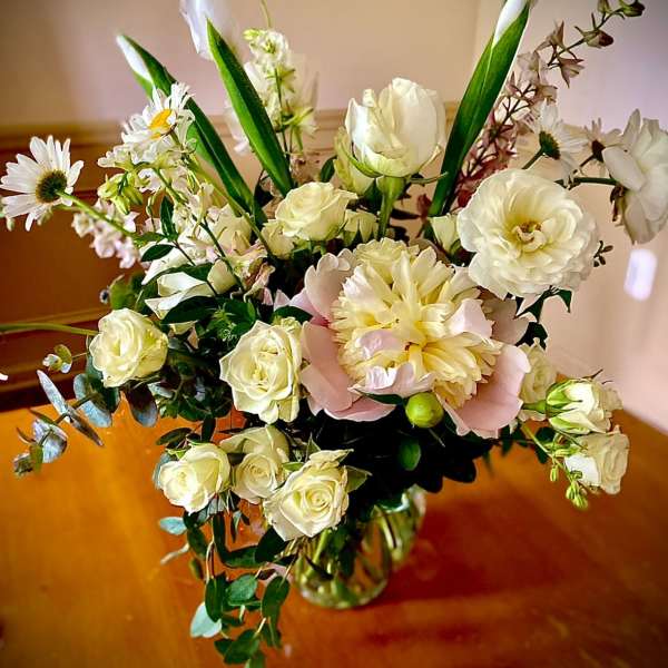 Tall mixed arrangement of white flowers with a blush peony in a clear glass vase