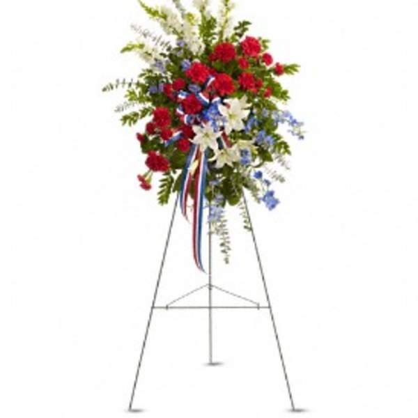 Tall red, white, and blue standing spray with lilies and carnations on a metal easel.