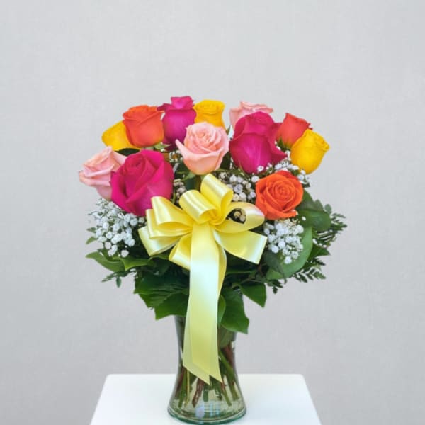 Bright mixed-color rose arrangement with baby's breath in a glass vase with a yellow bow