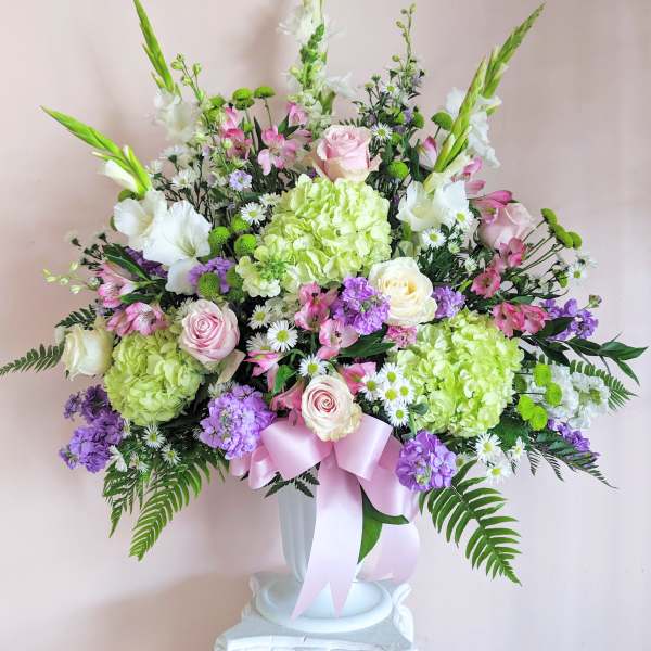 Large pastel floral arrangement in a white vase with a pink ribbon