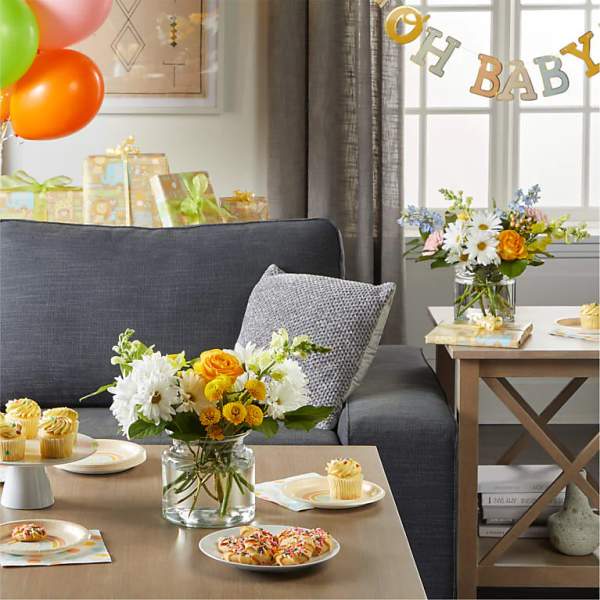 Flower arrangements in glass vases on a table with cupcakes and baby shower decor