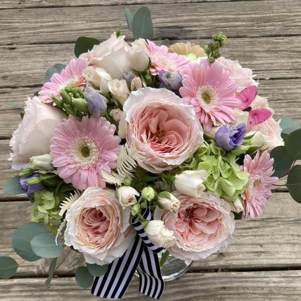 Bouquet of pink and white flowers in a clear vase with a striped ribbon