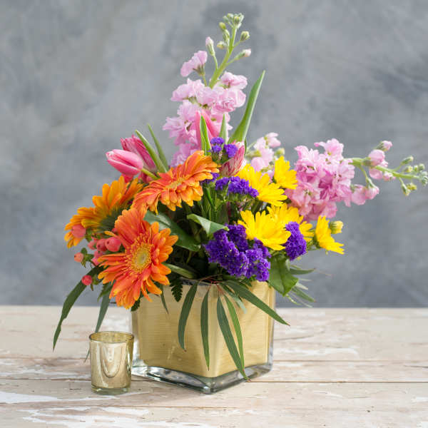 Colorful mixed bouquet in a square glass vase with a gold wrap.