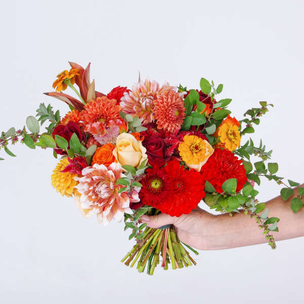 Handheld bouquet of red, orange, and cream flowers with greenery
