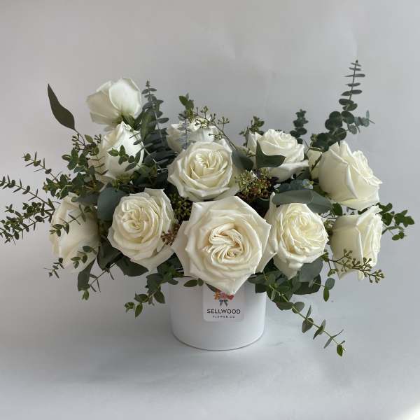 White roses arranged in a white vase with eucalyptus greenery
