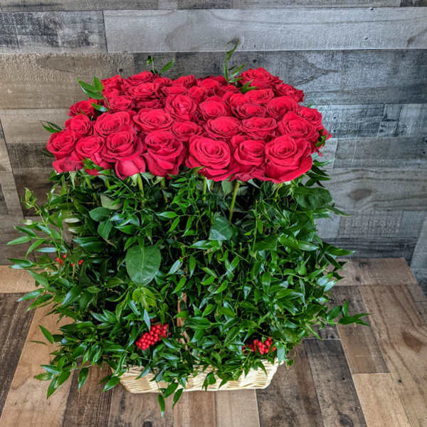 Tall arrangement of red roses atop dense green foliage in a rectangular basket