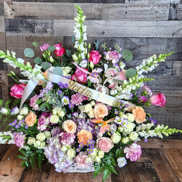 Large pastel sympathy basket with pink roses, snapdragons, and mixed flowers in a white woven basket