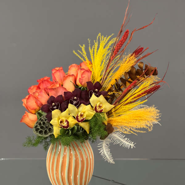 Bouquet of orange roses and yellow orchids in a striped vase