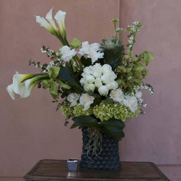 White calla lilies and roses arranged in a dark textured vase