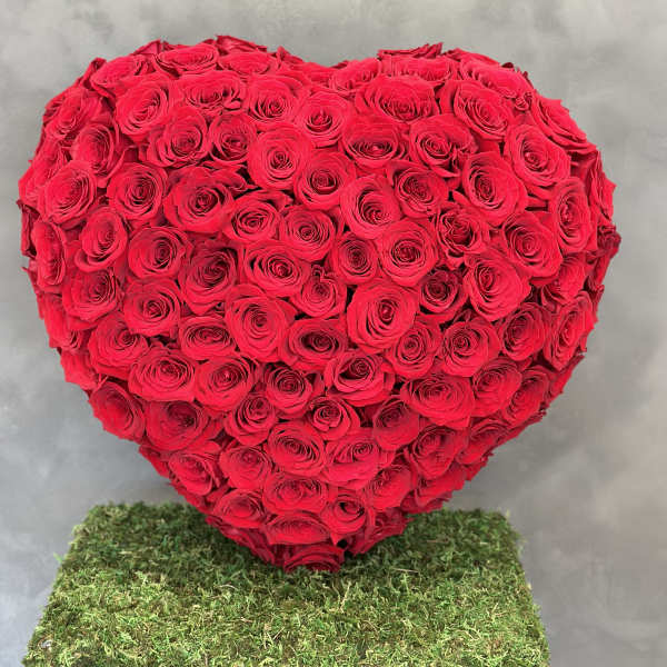 Heart-shaped arrangement of red roses on a moss-covered base