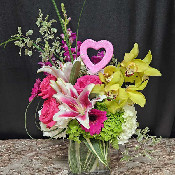 Bright mixed bouquet in a clear glass vase with a pink heart pick