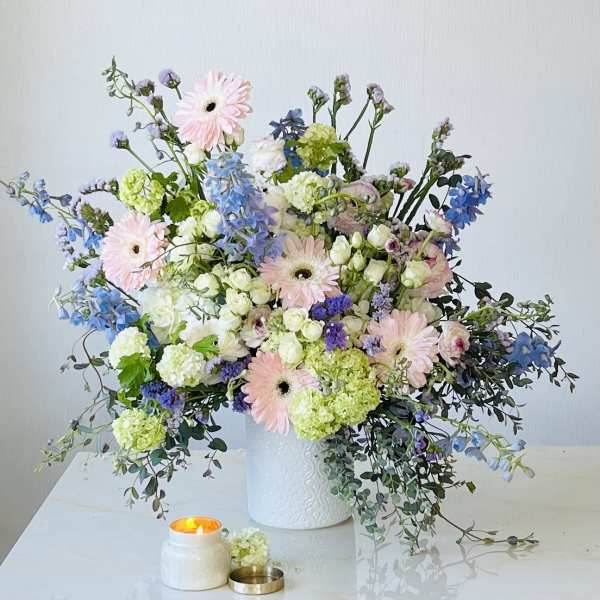 Pastel floral arrangement in a white vase with a lit candle nearby