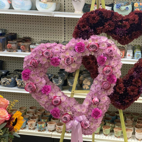 Two heart-shaped floral arrangements on stands, one pink and one burgundy.