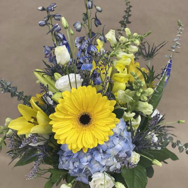 Mixed bouquet with yellow gerbera, blue hydrangea, and white blooms in a glass vase