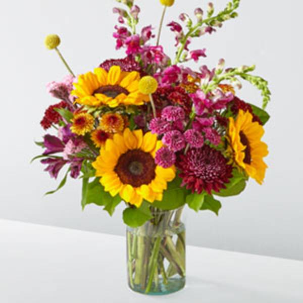 Bouquet of sunflowers, magenta blooms, and pink flowers in a glass vase