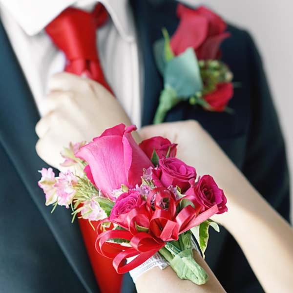 Pink rose corsage on a wrist with a matching boutonniere on a suit