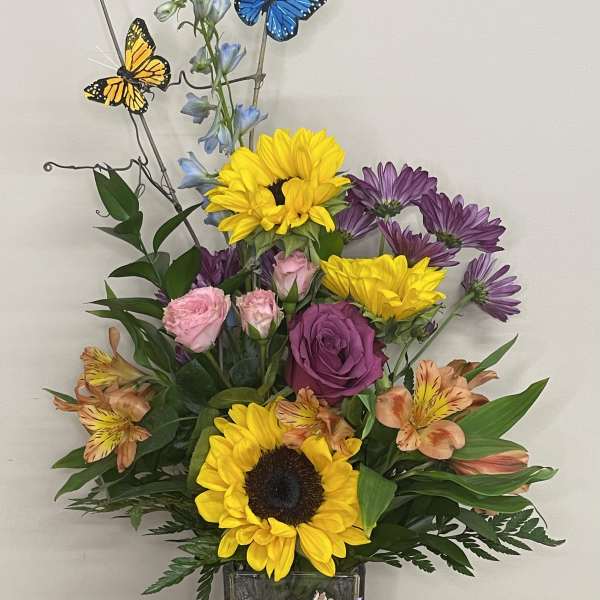 Mixed bouquet in a square glass vase with sunflowers, roses, and butterflies