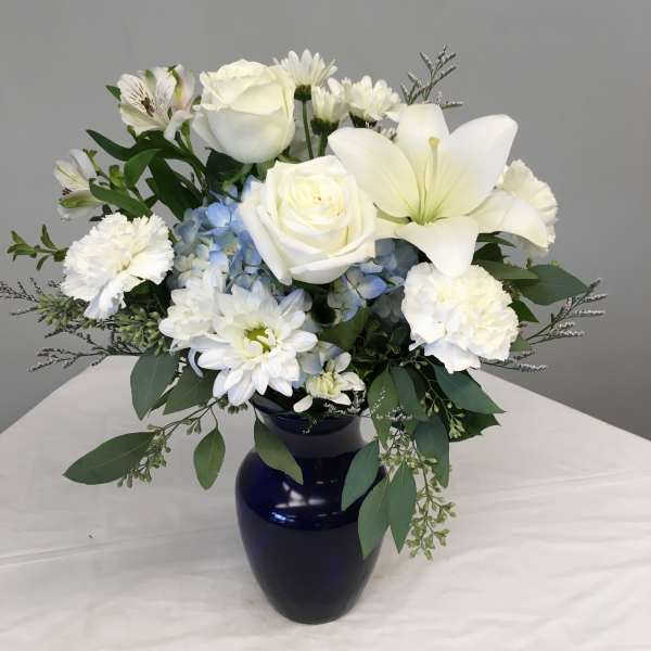 White roses, lilies, and daisies in a dark blue vase