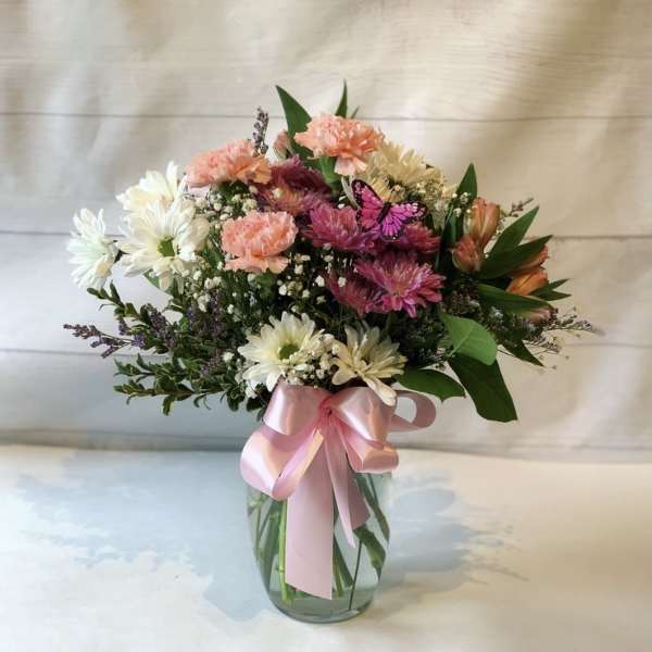 Mixed bouquet of pink, white, and peach flowers in a glass vase with a pink ribbon