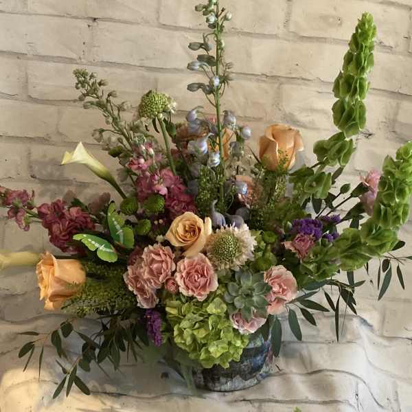 Mixed bouquet with peach roses, pink blooms, and tall green spikes in a vase