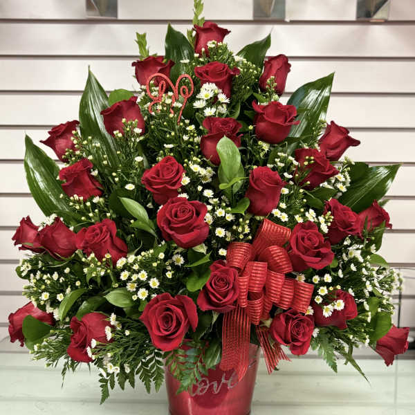 Red roses arranged in a red vase with small white filler flowers and ribbon