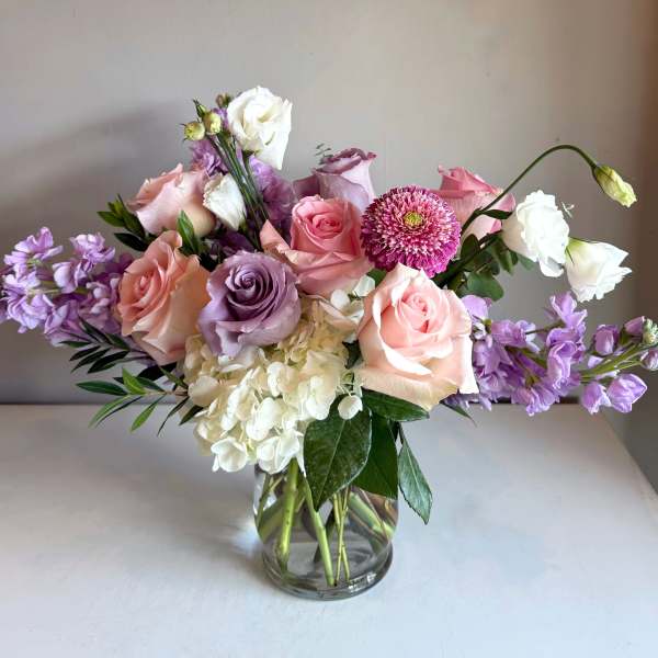 Mixed bouquet of pink, lavender, and white flowers in a glass vase