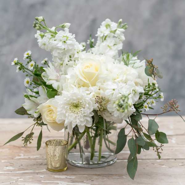 White floral arrangement in a clear glass vase with a small gold candle holder