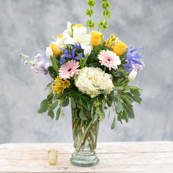 Mixed bouquet in a clear glass vase with yellow, white, pink, and purple flowers