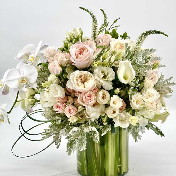 Pastel bouquet of roses, orchids, and calla lilies in a green glass vase