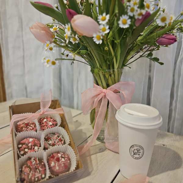 Tulip bouquet in a glass vase with a box of pink chocolates and a takeaway coffee cup