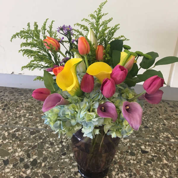 Colorful bouquet with tulips, calla lilies, and hydrangeas in a dark vase