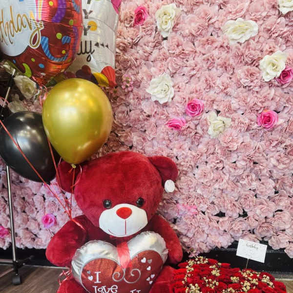 Red teddy bear with balloons beside a heart-shaped box of red roses