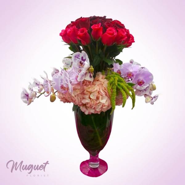 Red roses and orchids arranged in a tall glass vase